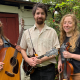 A guitarist, mandolin player, and fiddler stand side by side smiling.
