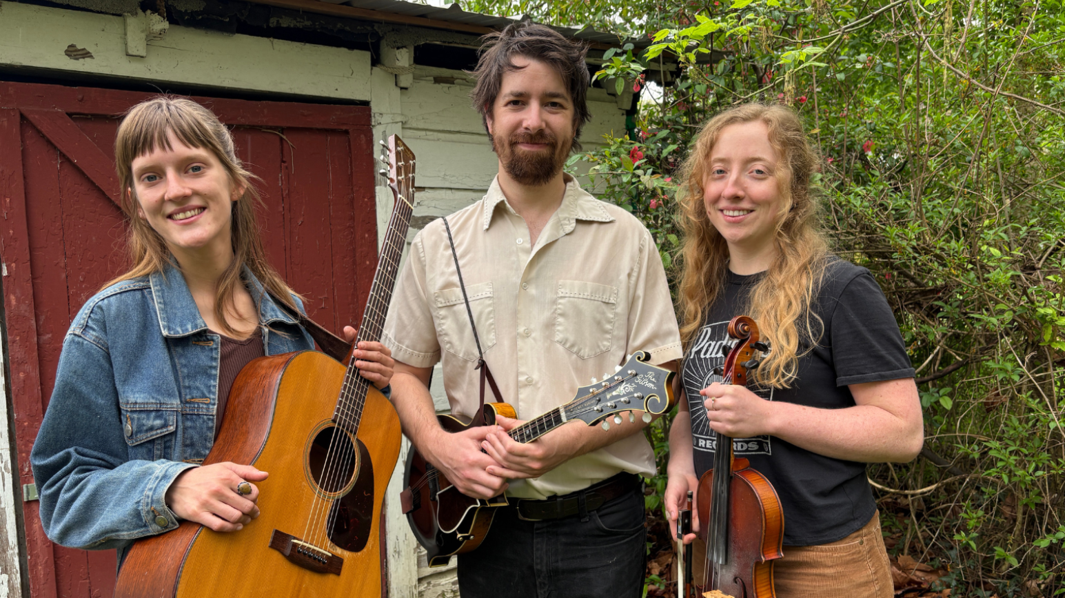 A guitarist, mandolin player, and fiddler stand side by side smiling.