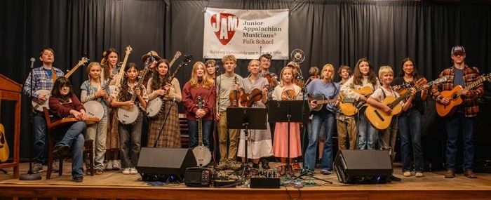 JAM students from the Folk School stand on stage with their instruments.